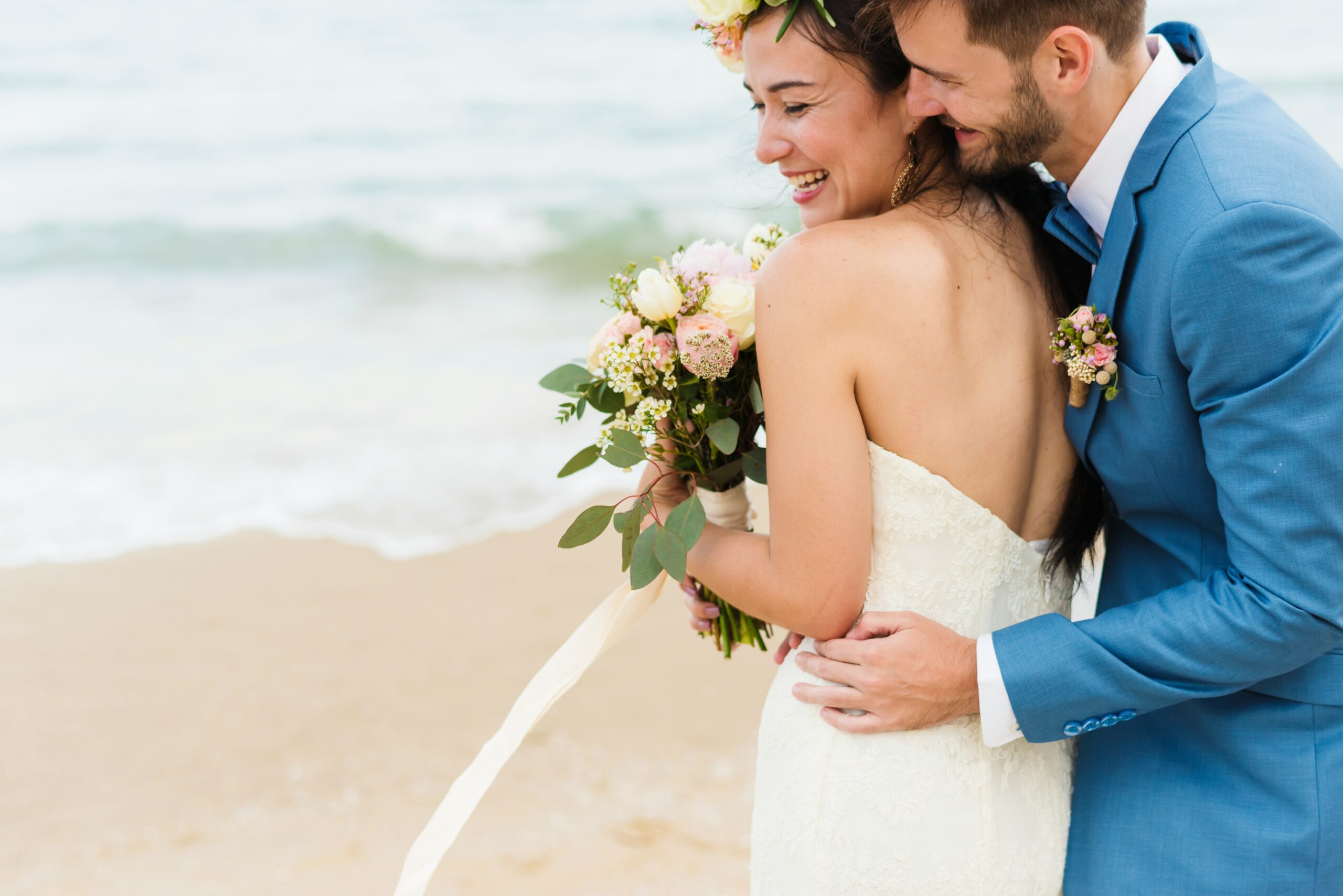 A bride and groom hold each other at the shoreline during a beach wedding ceremony