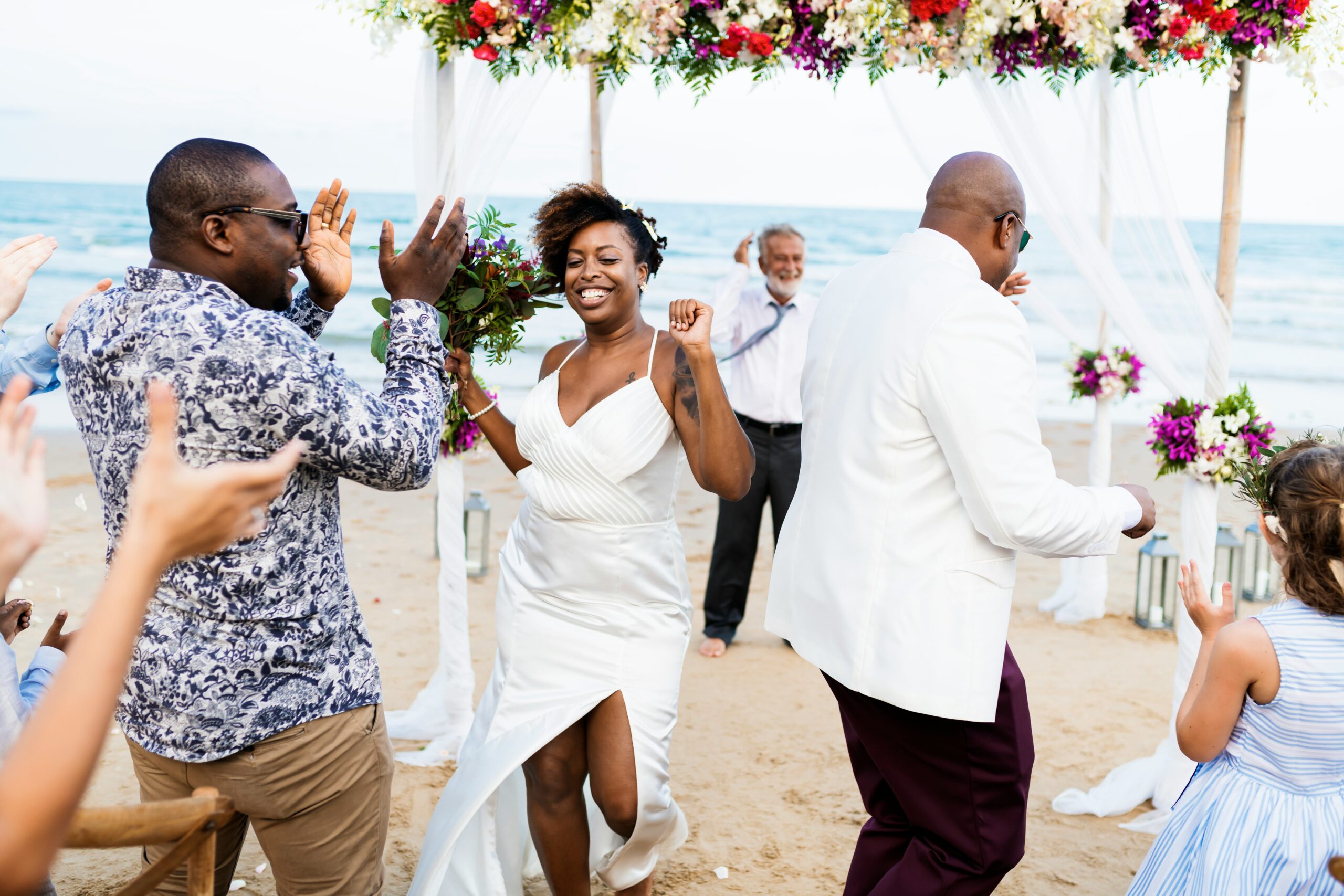 A newly married couple walk back down a sand aisle as guests cheer