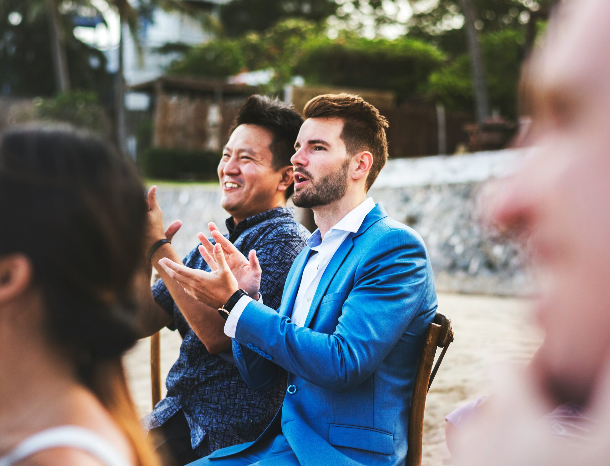 Two guests applaud and laugh during an outdoor beachside wedding ceremony