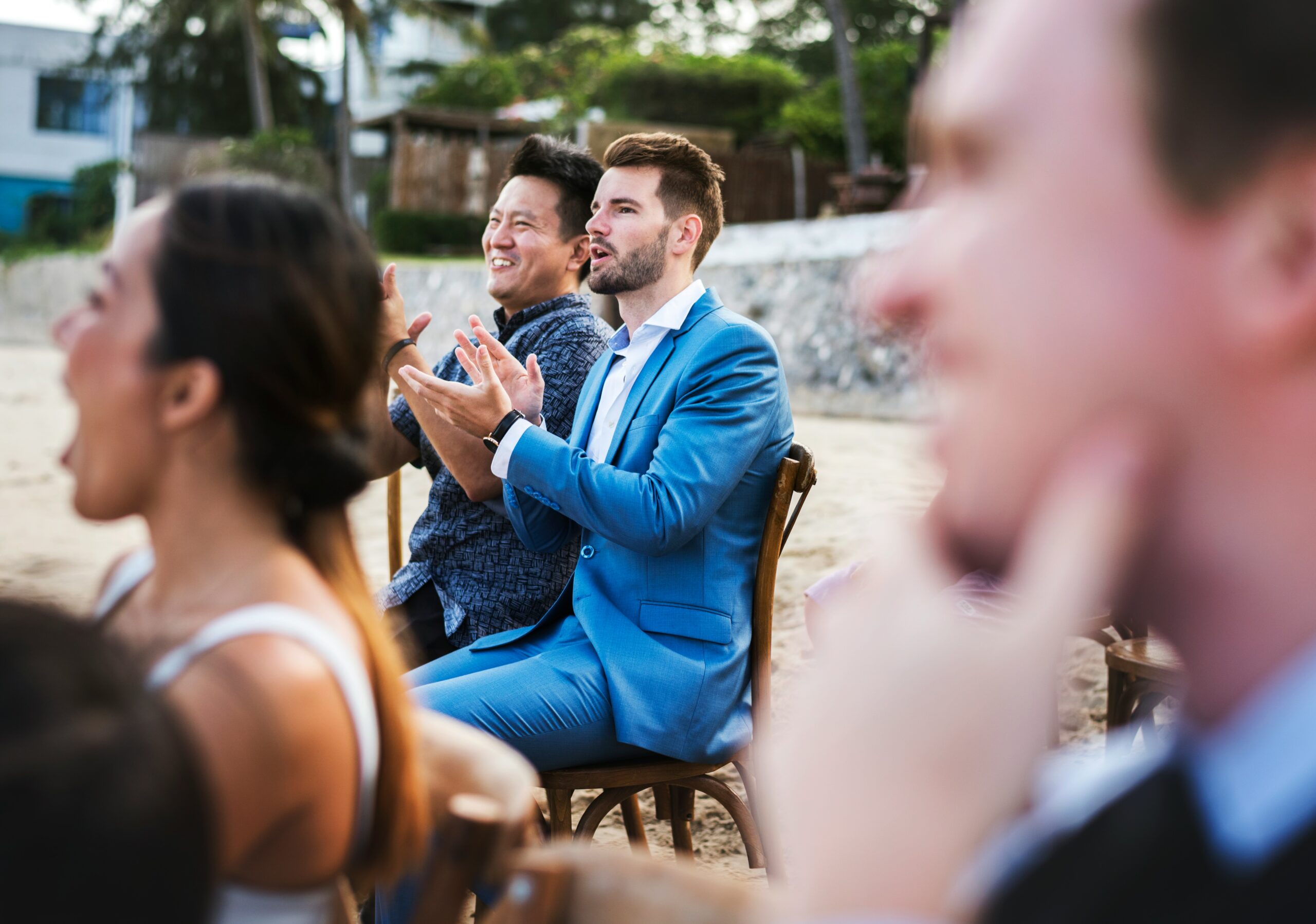 Wedding guests applaud from wooden chairs on the sand during a beach ceremony