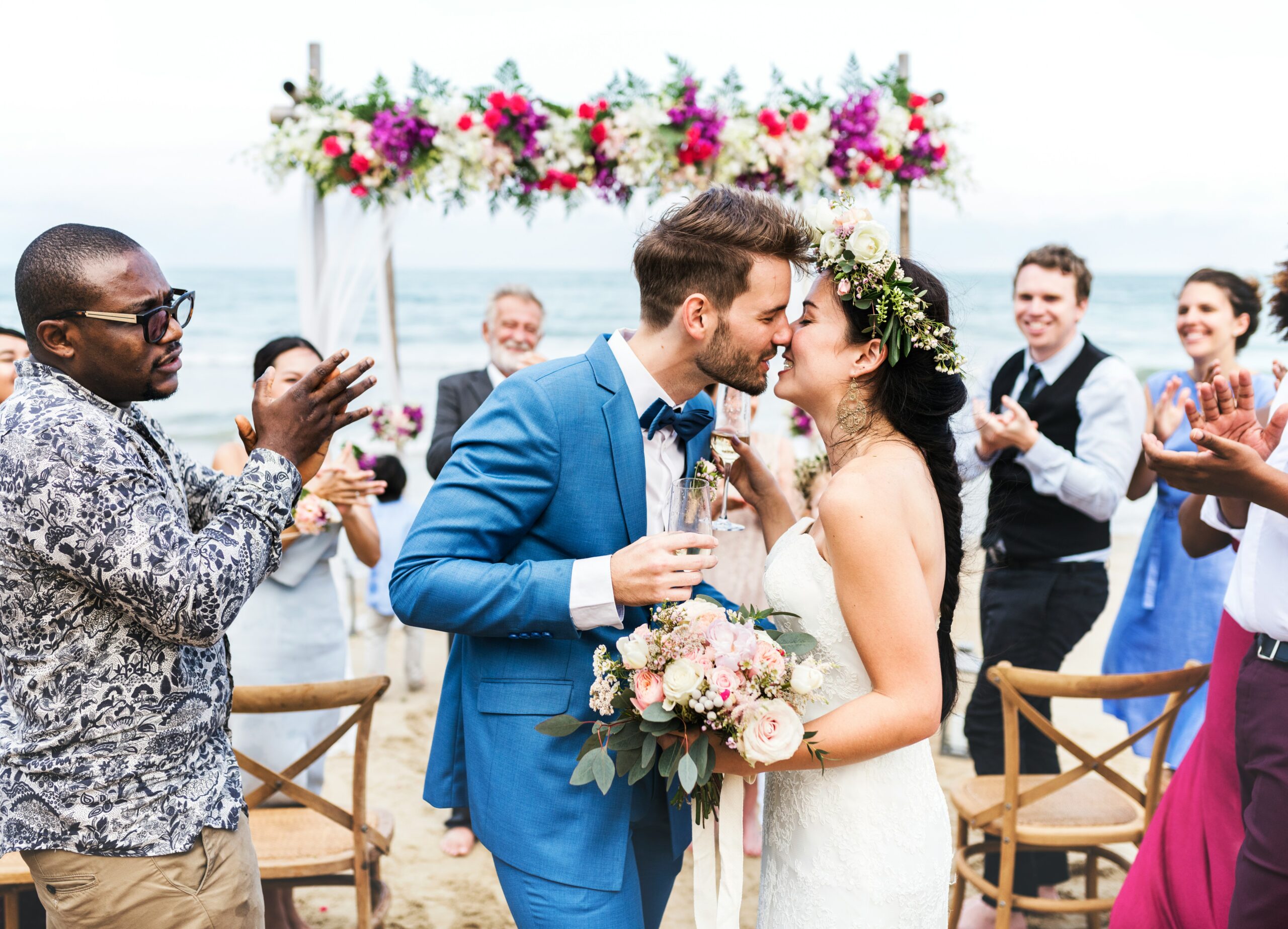 A bride and groom kiss surrounded by applauding guests at a beach reception