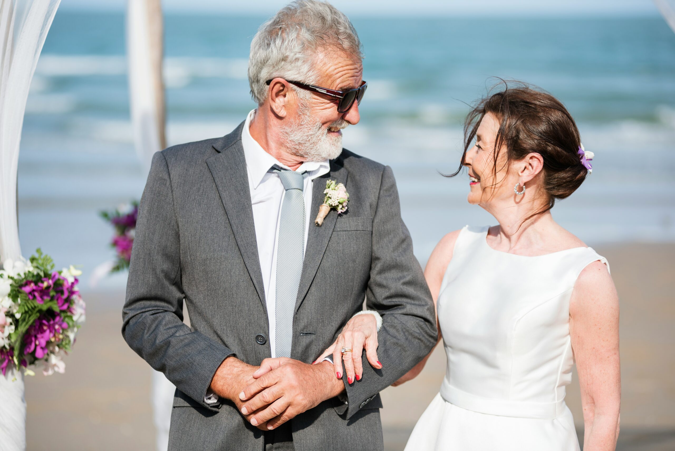 An older couple smile at each other during a beachfront wedding ceremony